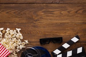 Clapperboard, film reel and popcorn on wooden background, top view